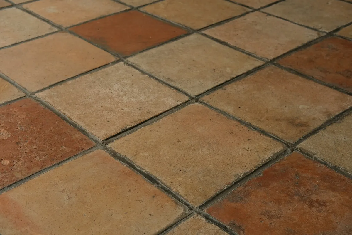 A floor of square terracotta tiles in mixed shades with dark grout lines A floor of square terracotta tiles in mixed shades with dark grout lines