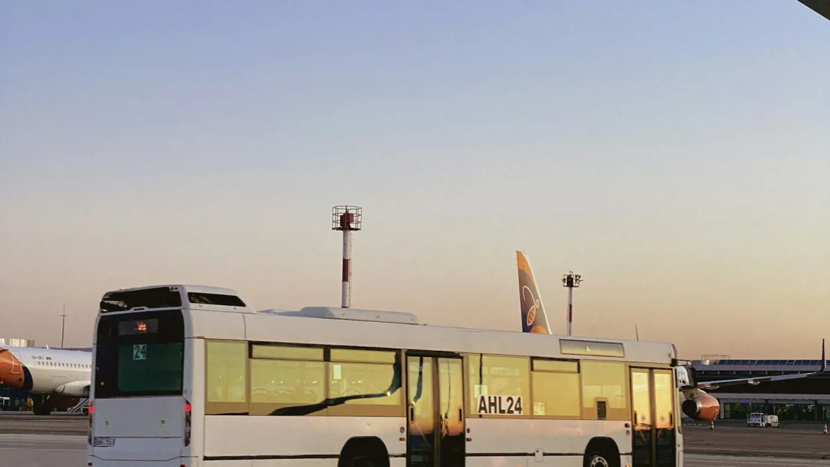 A white bus at an airport at sunset with aircraft in the background