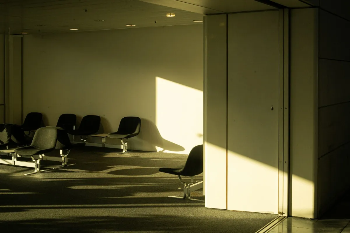 Empty seats in an airport waiting area, lit by low sunlight falling across the wall and floor Empty seats in an airport waiting area, lit by low sunlight falling across the wall and floor