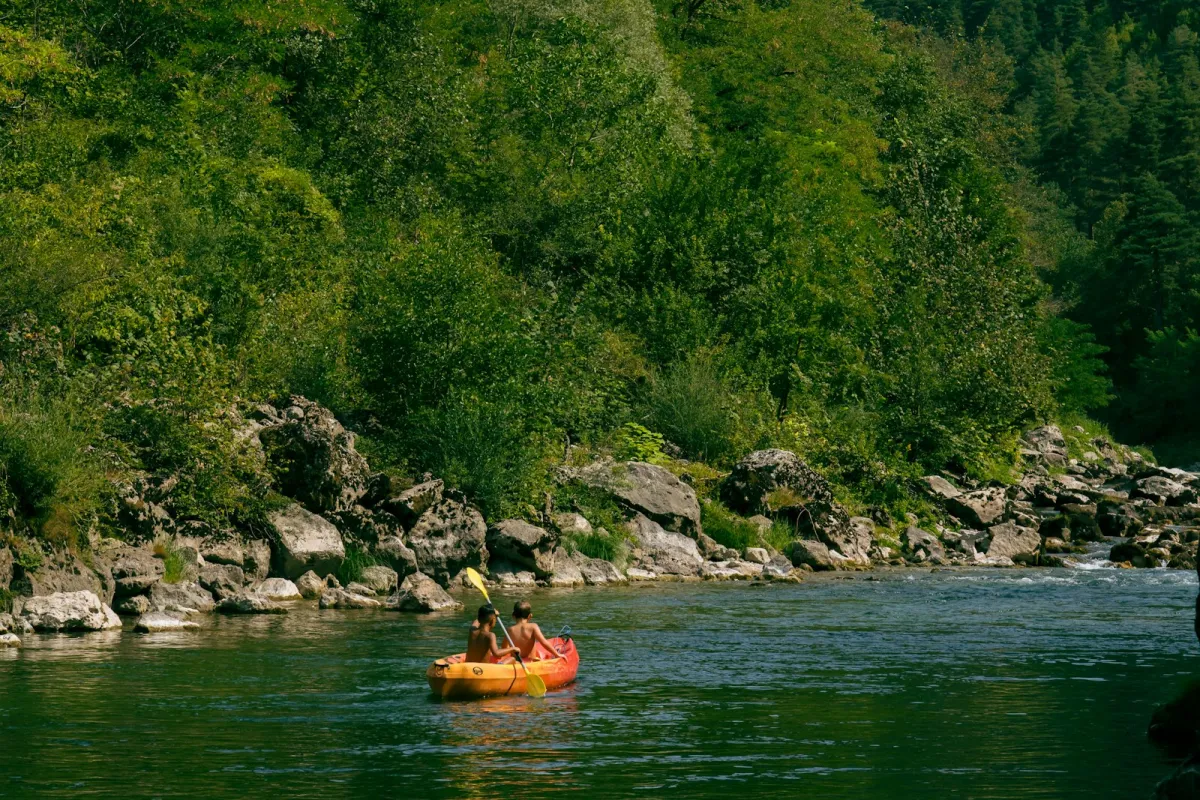 Two people paddling an orange kayak down a tree-lined river Two people paddling an orange kayak down a tree-lined river