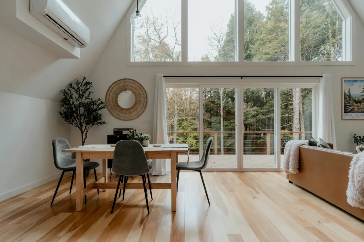 A bright open-plan room with light hardwood floors, a wooden dining table and large windows A bright open-plan room with light hardwood floors, a wooden dining table and large windows