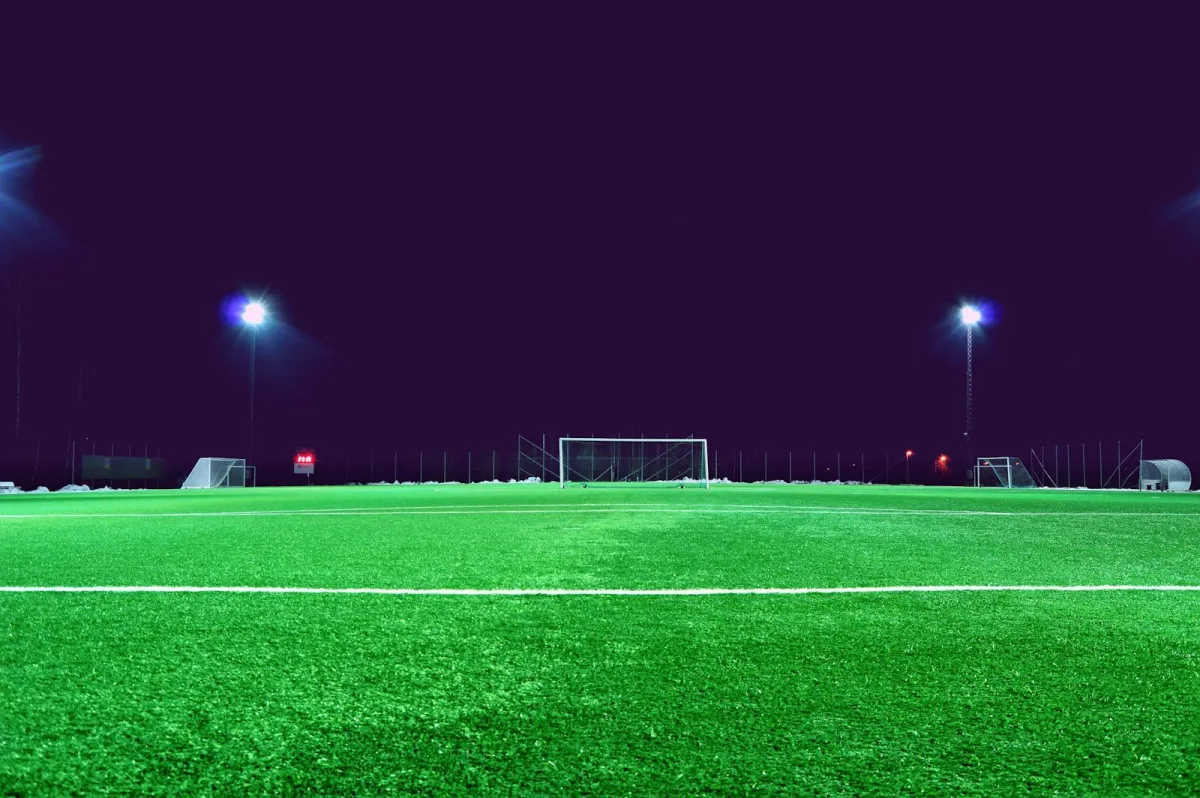 An empty floodlit football pitch at night with a goal in the distance An empty floodlit football pitch at night with a goal in the distance