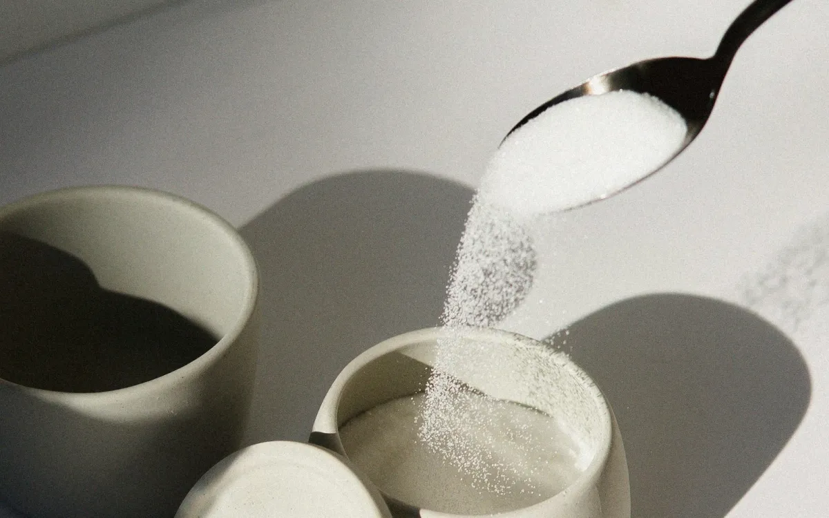 Sugar pouring from a spoon into a white ceramic cup Sugar pouring from a spoon into a white ceramic cup
