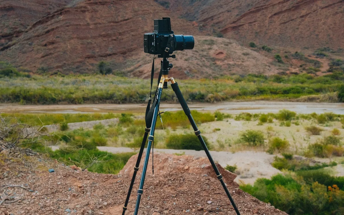 Film camera on a tripod in front of a red mountain valley