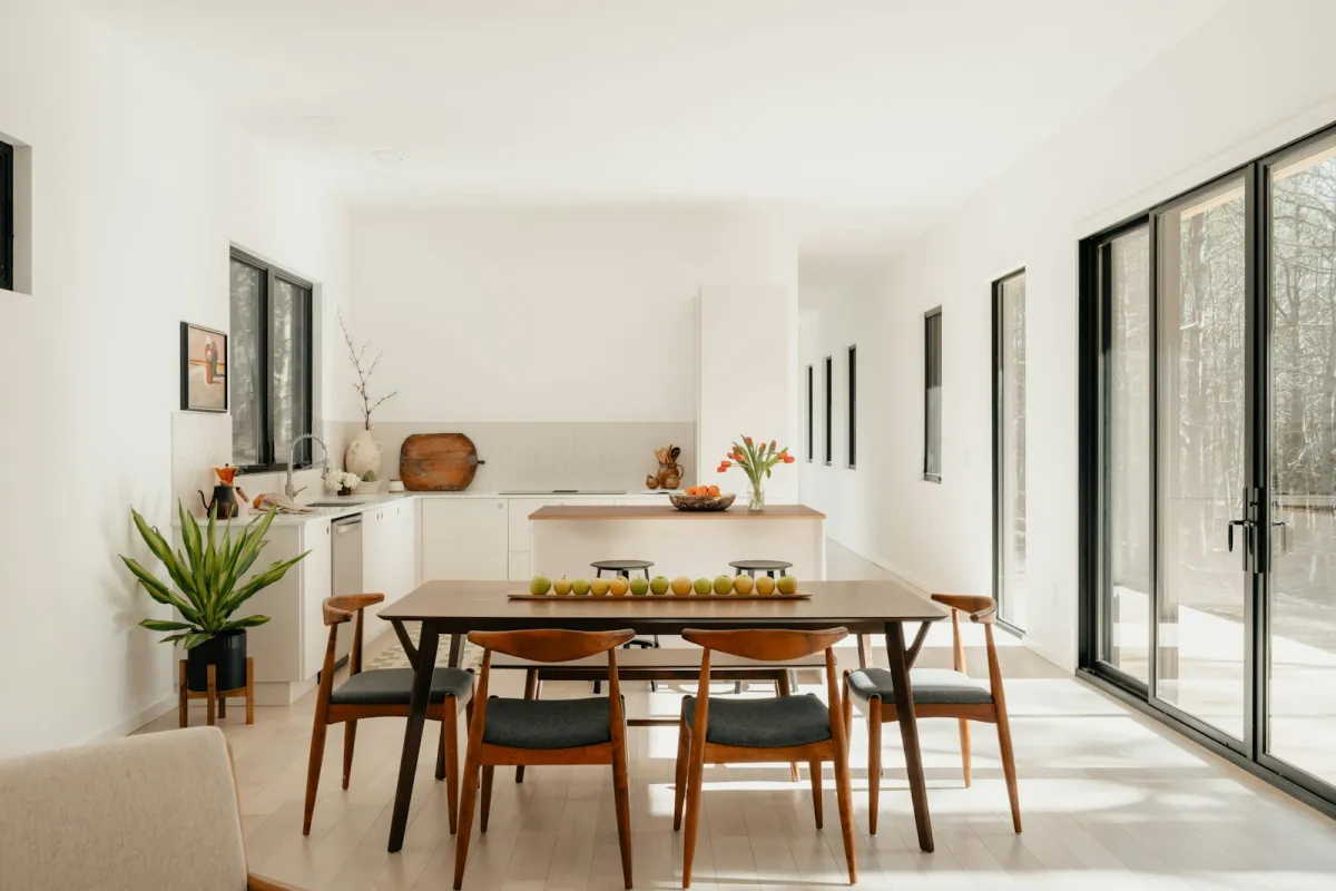 Bright modern dining room with a wooden table and chairs in front of a white kitchen Bright modern dining room with a wooden table and chairs in front of a white kitchen