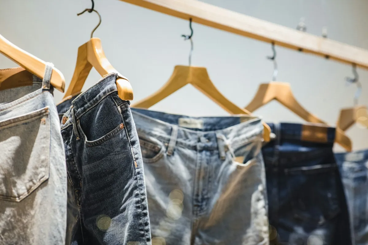 Pairs of blue jeans hanging on wooden hangers from a rail