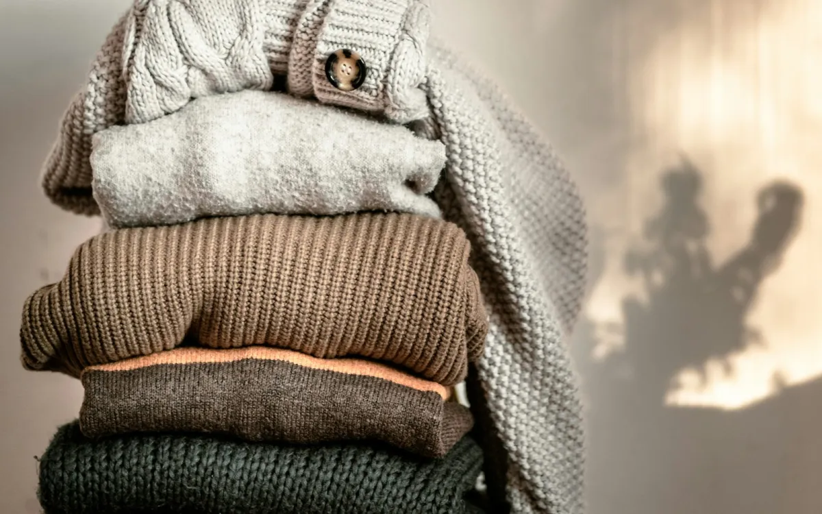 A stack of folded knitted jumpers in grey, brown and green A stack of folded knitted jumpers in grey, brown and green