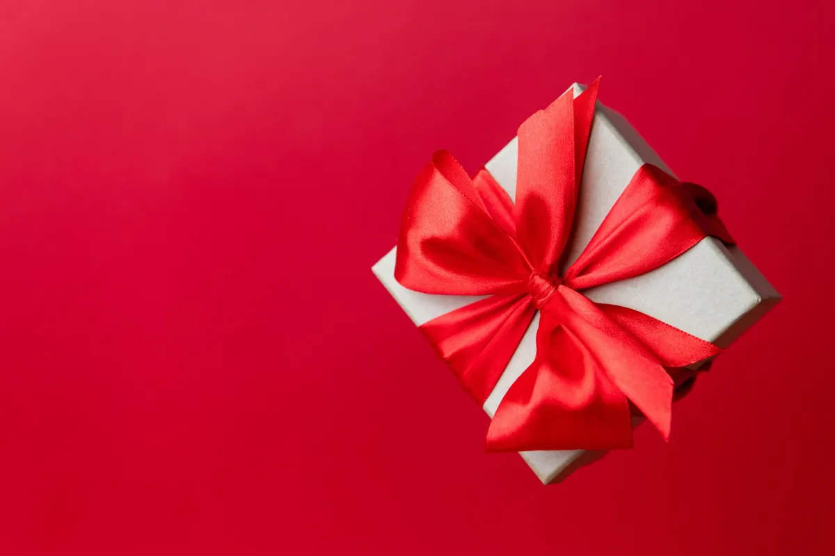 A small white gift box tied with a red satin bow on a plain red background A small white gift box tied with a red satin bow on a plain red background