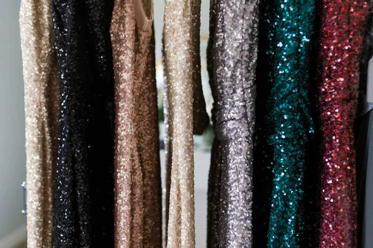 A row of sequin dresses in gold, black, silver, teal and red hanging on a rail