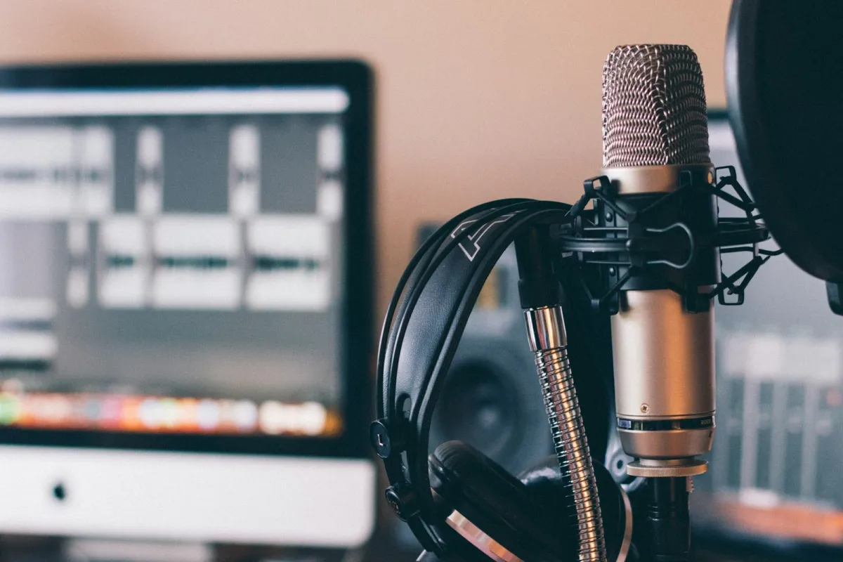 Studio headphones hanging on a microphone in front of a computer screen showing audio tracks Studio headphones hanging on a microphone in front of a computer screen showing audio tracks