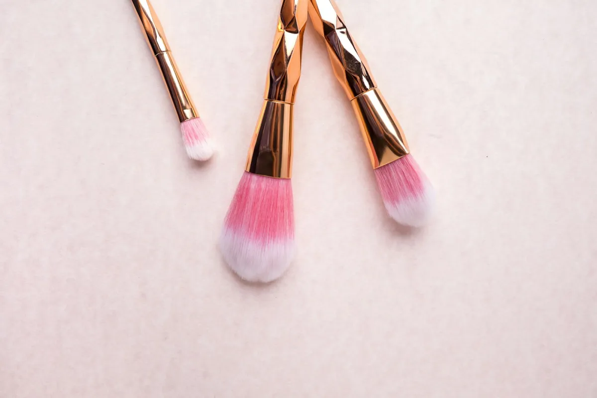 Three pink make-up brushes with gold handles on a pale pink surface