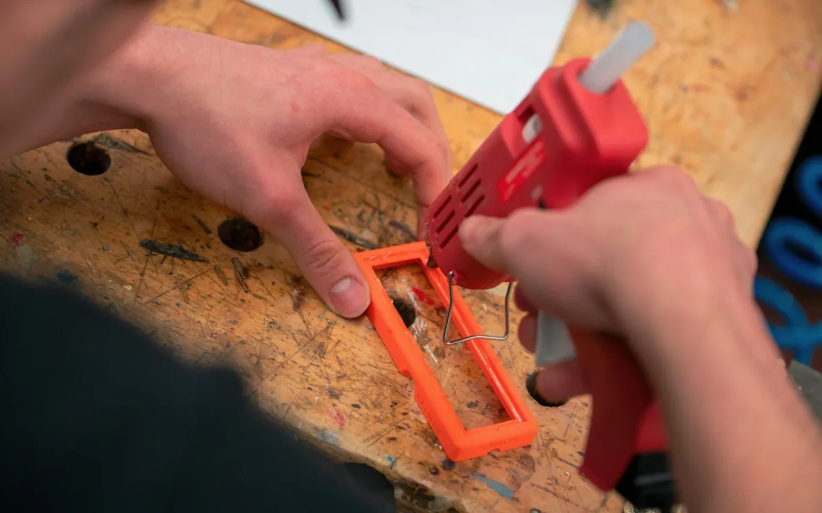 Hands using a hot glue gun on a craft project on a wooden workbench Hands using a hot glue gun on a craft project on a wooden workbench
