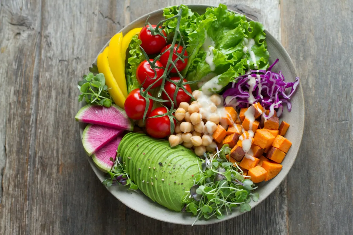 A colourful bowl of salad with chickpeas, avocado, sweet potato and tomatoes on a wooden table