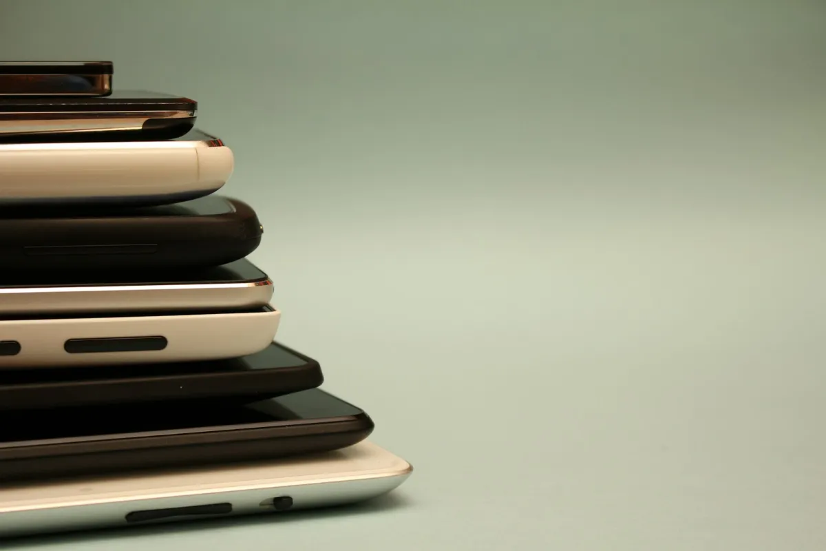 A stack of smartphones and tablets seen from the side against a pale green background A stack of smartphones and tablets seen from the side against a pale green background