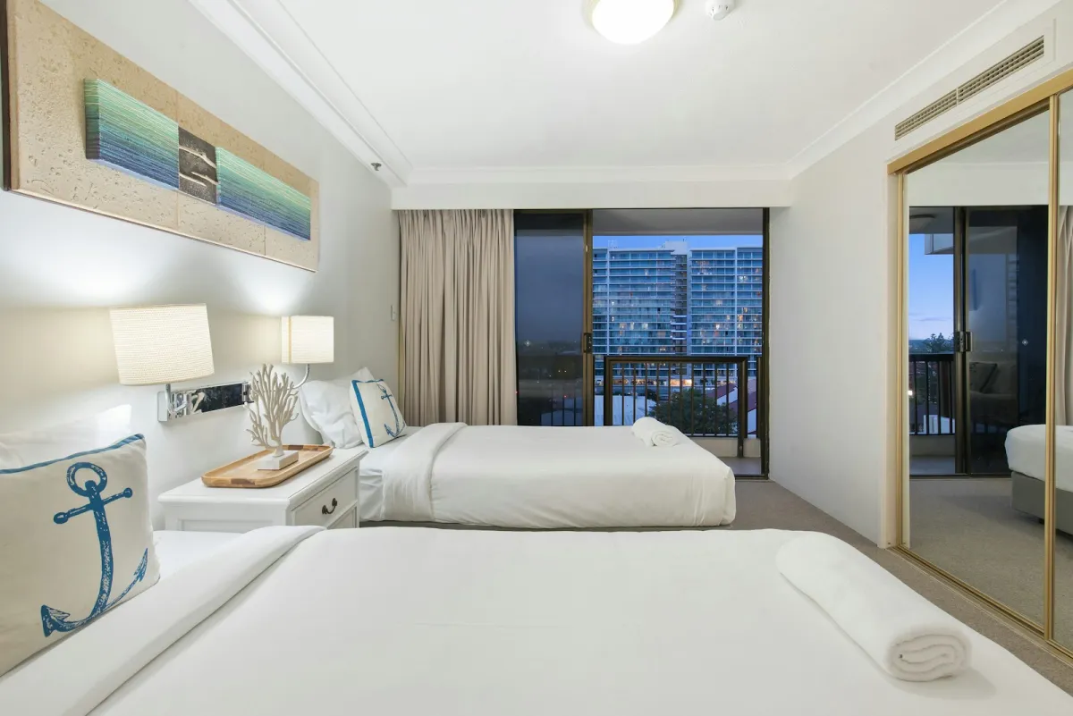 Two made-up beds with white linen in a bright apartment bedroom