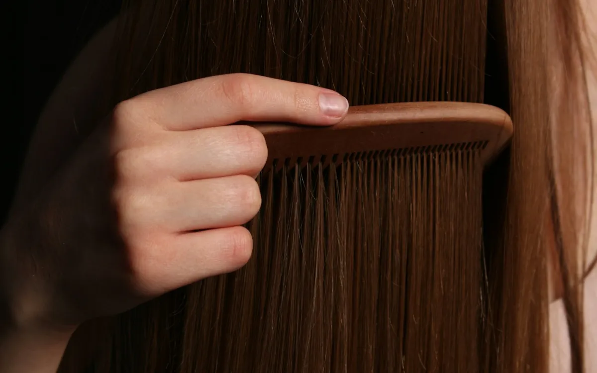 Hand running a wooden comb through long brown hair Hand running a wooden comb through long brown hair