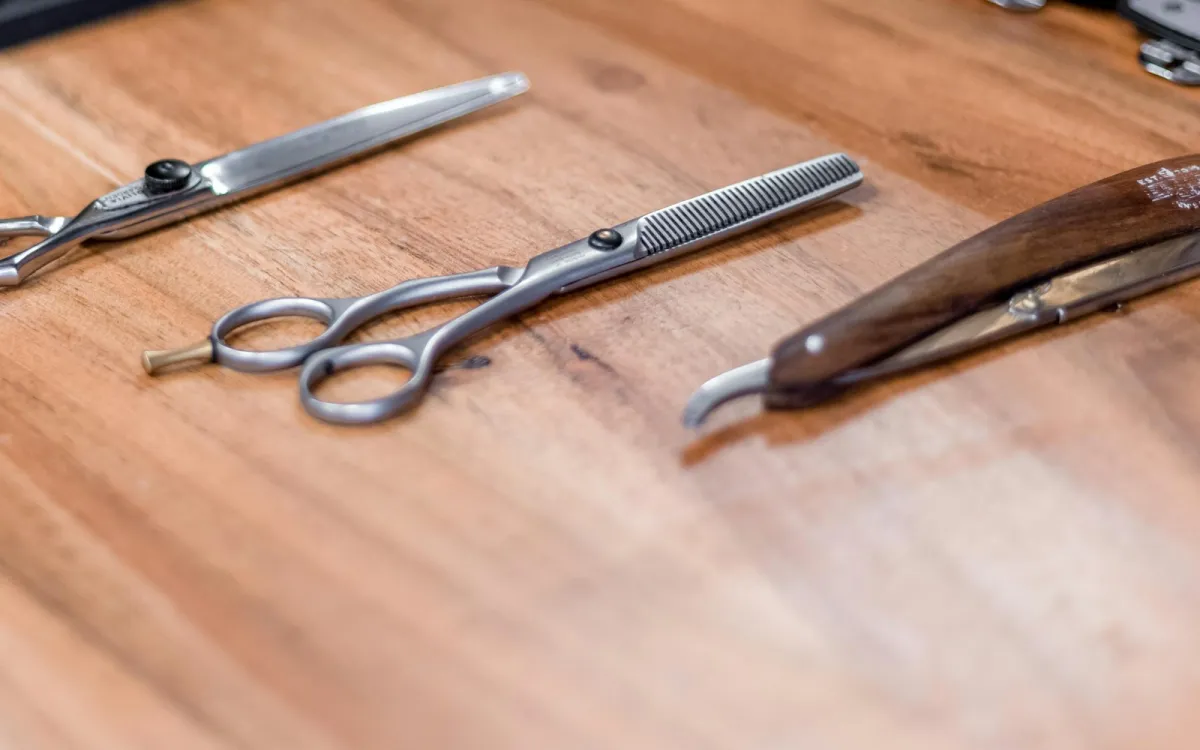 Hairdressing scissors, thinning scissors and a straight razor laid out on a wooden salon counter