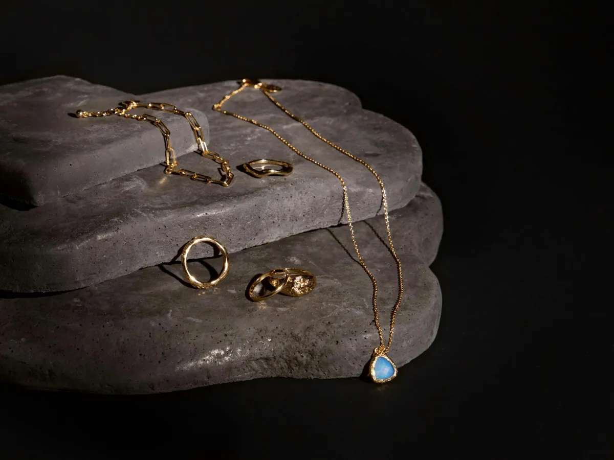Gold rings, a chain bracelet and a blue gemstone pendant necklace laid on grey stone Gold rings, a chain bracelet and a blue gemstone pendant necklace laid on grey stone