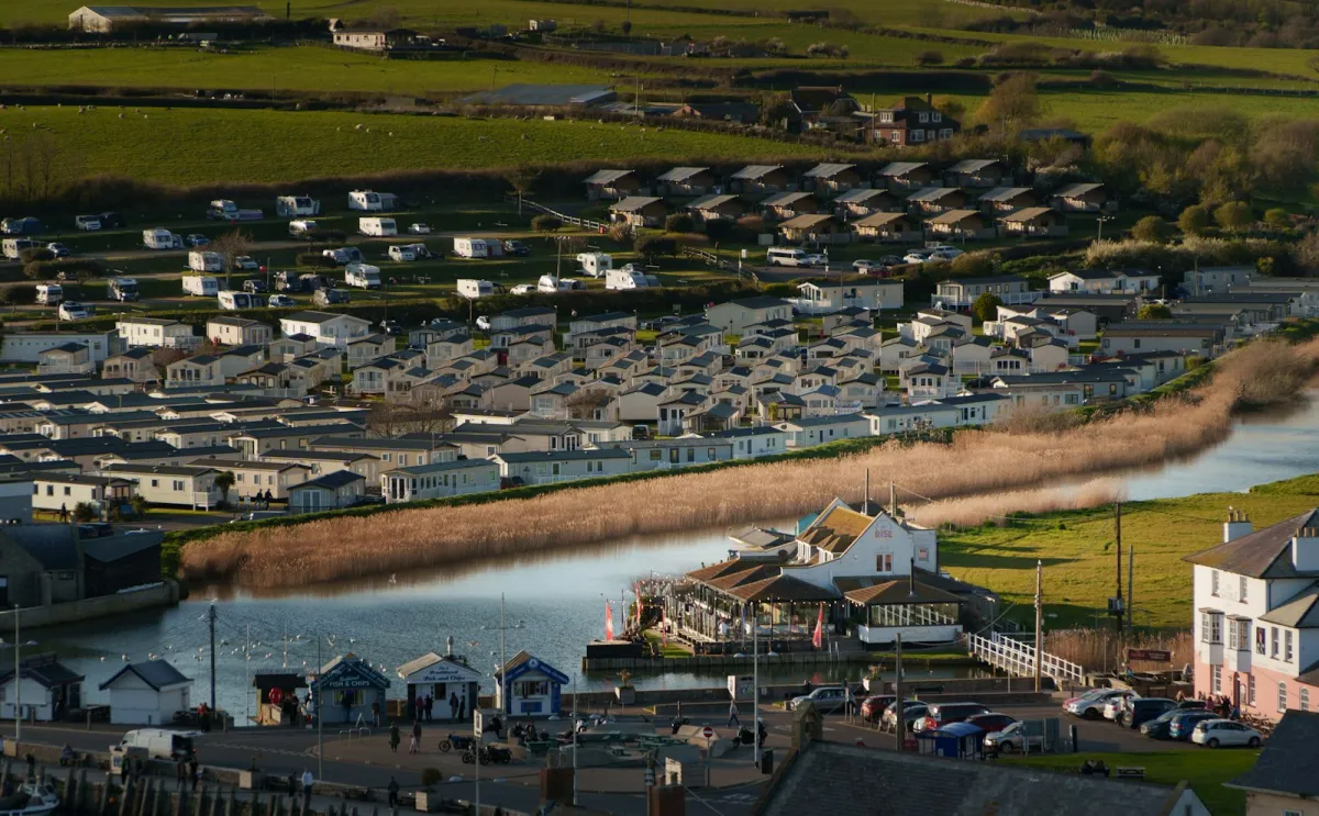 Rows of static caravans at a holiday park beside a river and green hills