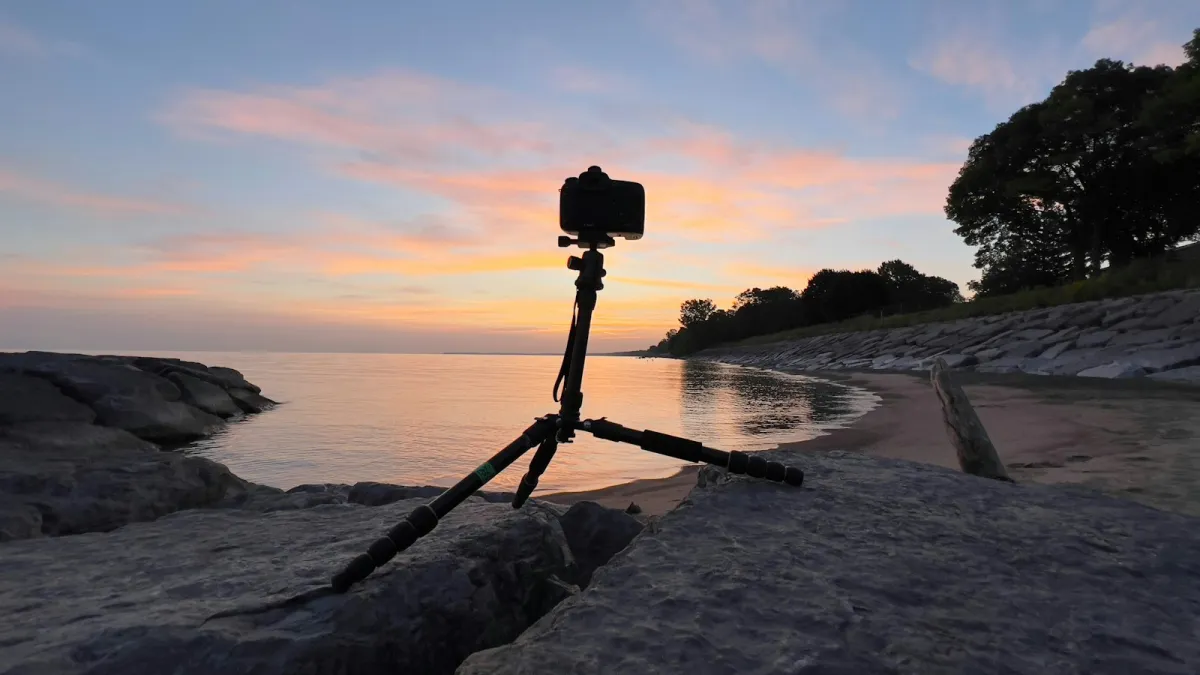 Camera on a travel tripod set up on rocks by a lake at sunset Camera on a travel tripod set up on rocks by a lake at sunset