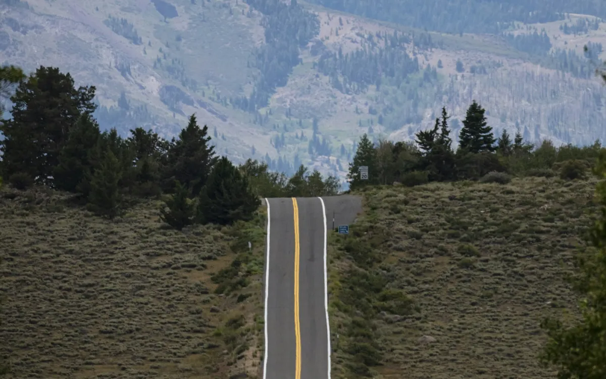 An empty road climbing over a hill towards forested mountains An empty road climbing over a hill towards forested mountains