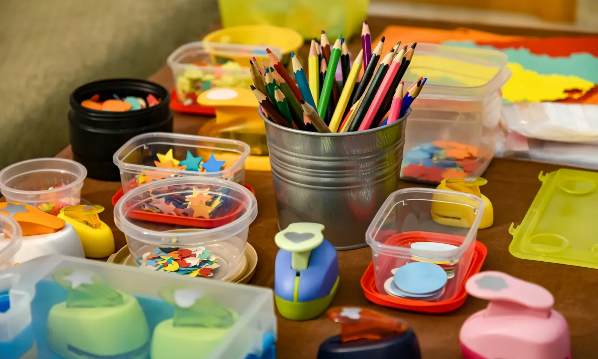 Coloured pencils in a metal pot surrounded by tubs of paper shapes and craft punches