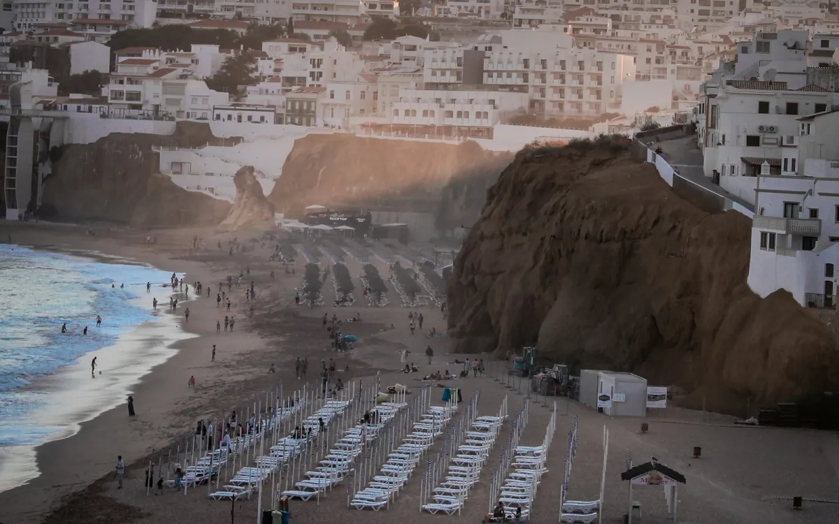 Rows of sun loungers on a sandy beach below a whitewashed town on the cliffs Rows of sun loungers on a sandy beach below a whitewashed town on the cliffs