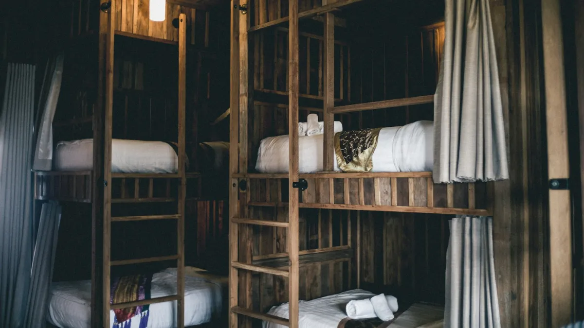 Wooden bunk beds with white bedding and curtains in a hostel dorm