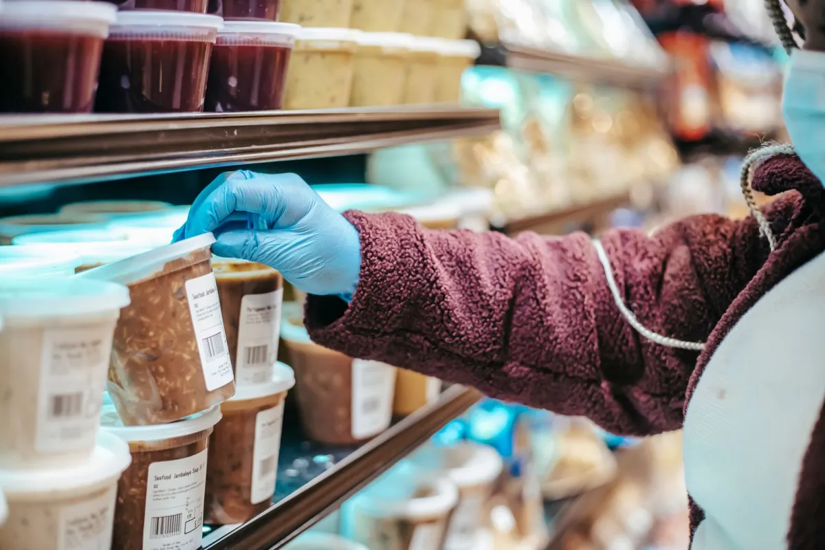 A shopper's gloved hand picking a tub from a chilled supermarket shelf A shopper's gloved hand picking a tub from a chilled supermarket shelf