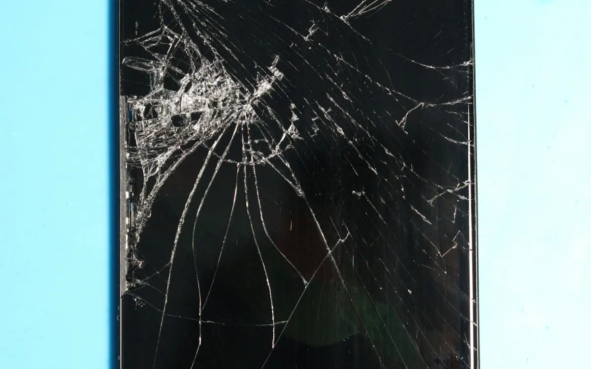 A smartphone with a badly cracked screen lying on a pale blue surface