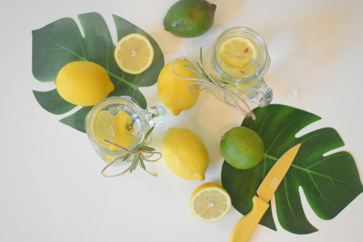 Glass jars of water with lemon slices surrounded by lemons, limes and green leaves