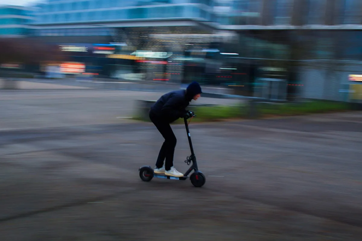 Rider in a dark jacket on a black kick scooter with motion-blurred city buildings behind