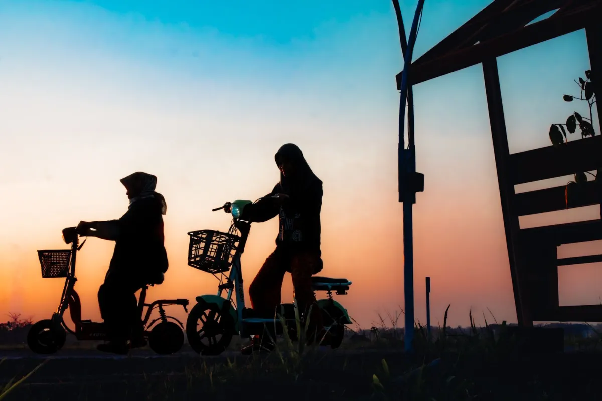 Two riders on seated electric scooters silhouetted against a sunset sky Two riders on seated electric scooters silhouetted against a sunset sky