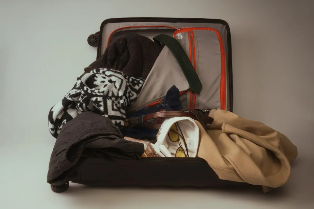 An open suitcase overflowing with jumpers, a coat, a belt and sunglasses An open suitcase overflowing with jumpers, a coat, a belt and sunglasses