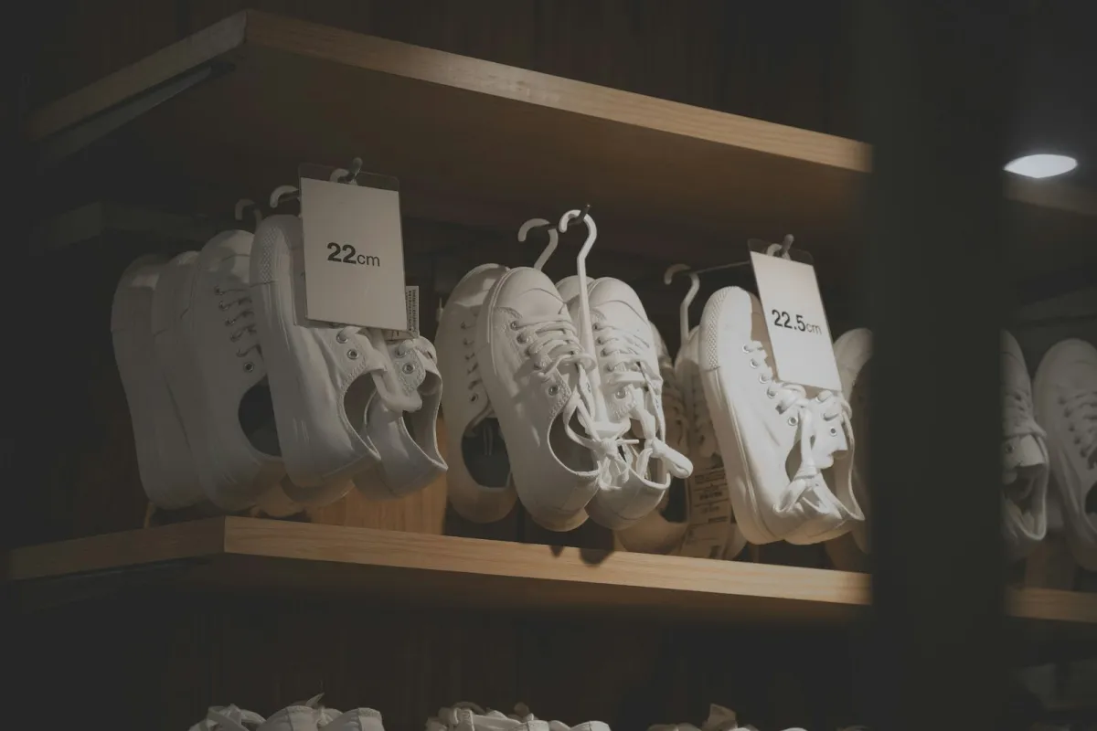 White canvas trainers hanging on a wooden shop shelf with size tags White canvas trainers hanging on a wooden shop shelf with size tags