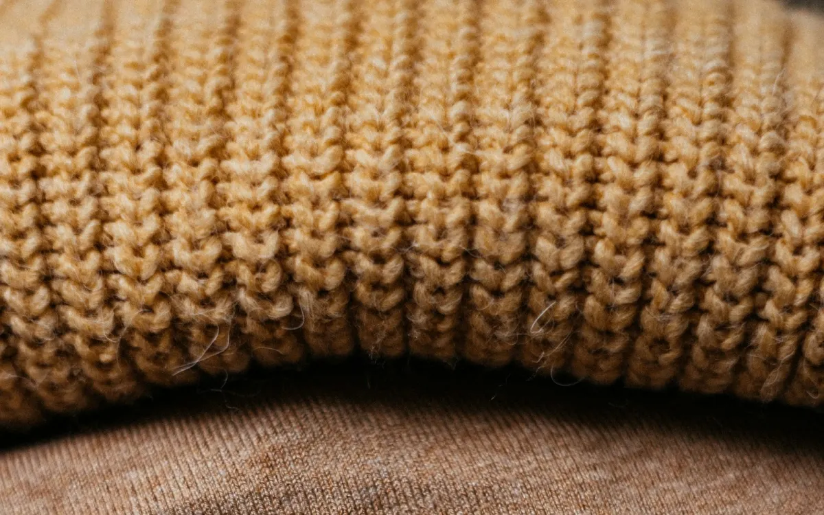 Close-up of a chunky mustard knit jumper folded on top of a brown sweater