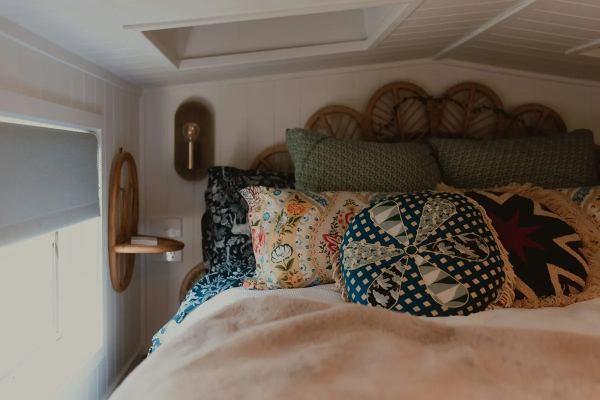 A cosy bed piled with patterned cushions and a soft cream throw under a sloping ceiling