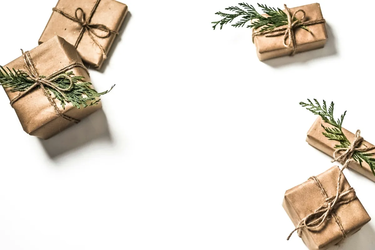 Four small gifts wrapped in brown paper, tied with string and sprigs of greenery, on a white surface Four small gifts wrapped in brown paper, tied with string and sprigs of greenery, on a white surface