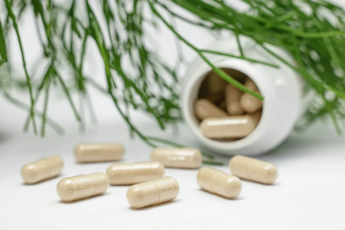 Beige capsules spilling from a white bottle beside green foliage Beige capsules spilling from a white bottle beside green foliage