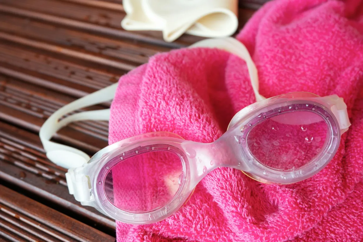 Swimming goggles and a swim cap on a pink towel on a wooden pool deck Swimming goggles and a swim cap on a pink towel on a wooden pool deck
