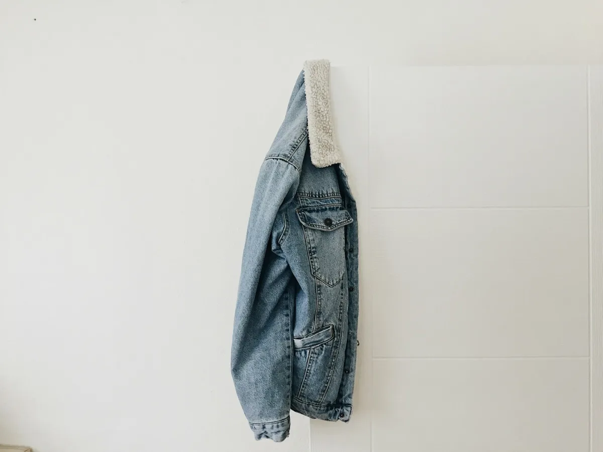 A light-wash denim jacket with a fleece collar hanging on a white door A light-wash denim jacket with a fleece collar hanging on a white door