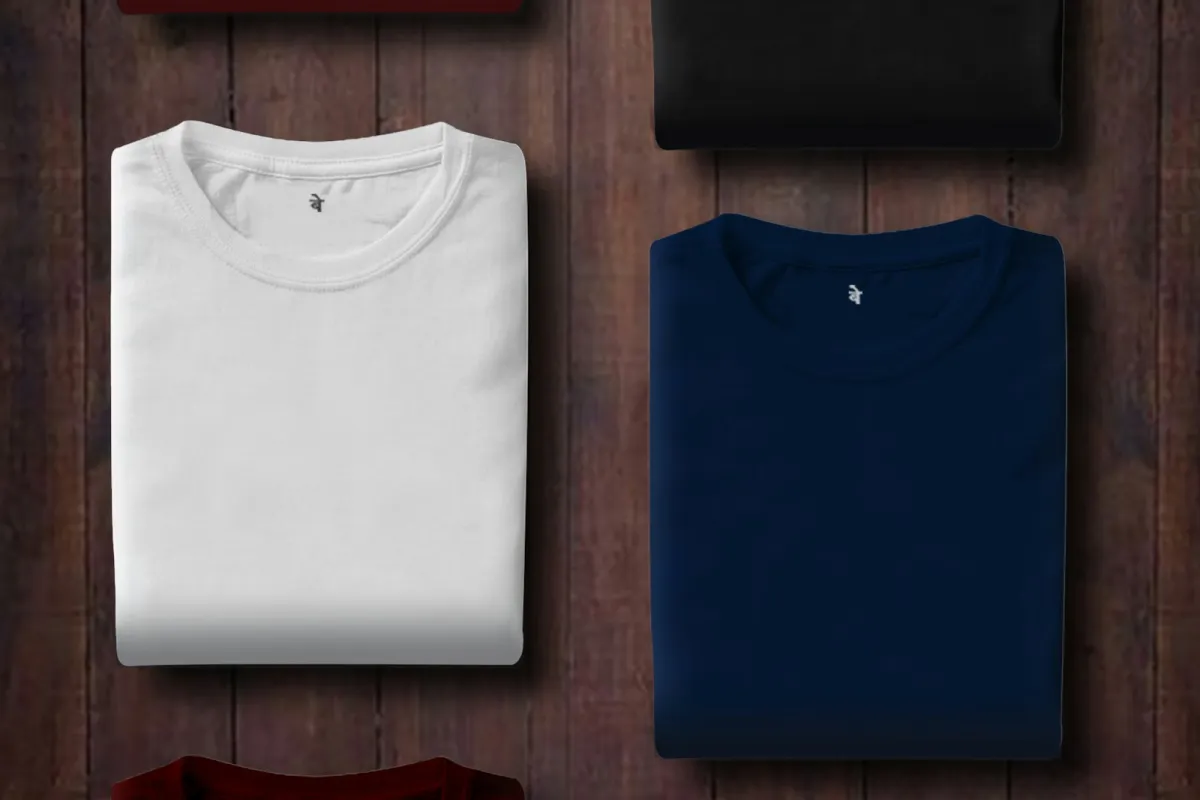 Plain folded T-shirts in white, navy, black and maroon on a wooden surface Plain folded T-shirts in white, navy, black and maroon on a wooden surface