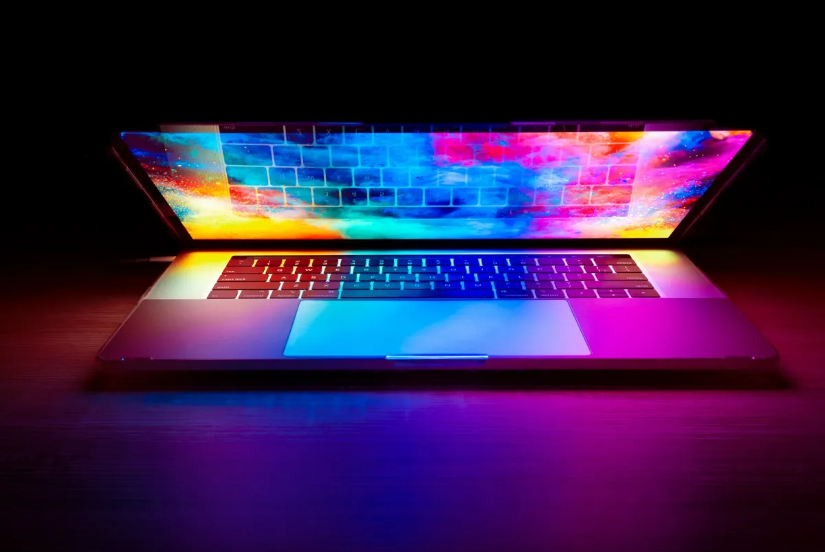 A half-open laptop glowing with a colourful screen on a dark desk
