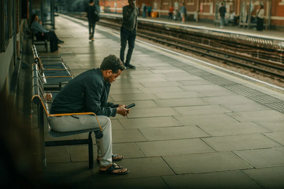 A man on a station platform bench checking his phone