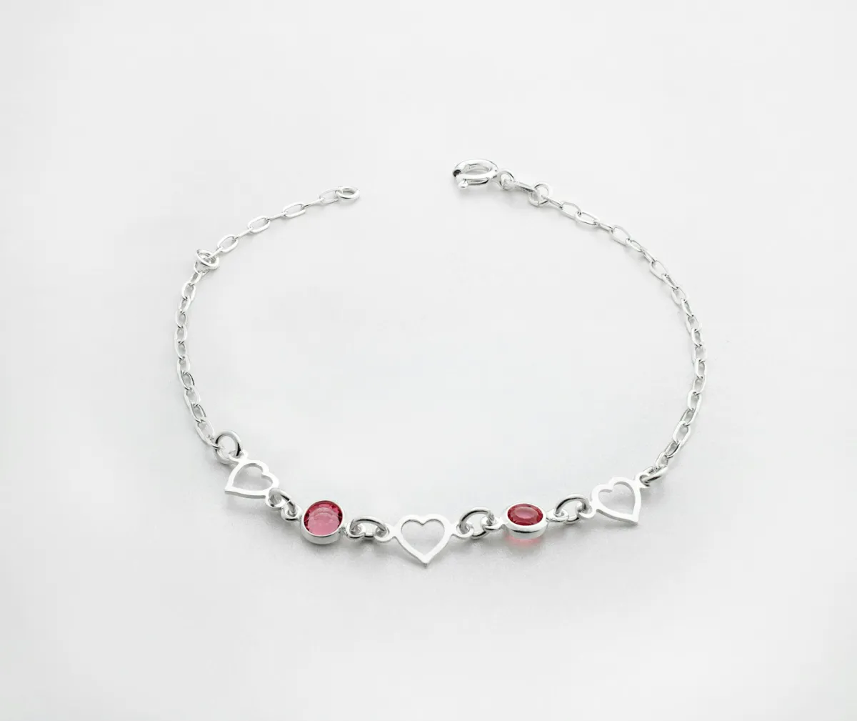 A silver bracelet with heart links and two red stones on a white background