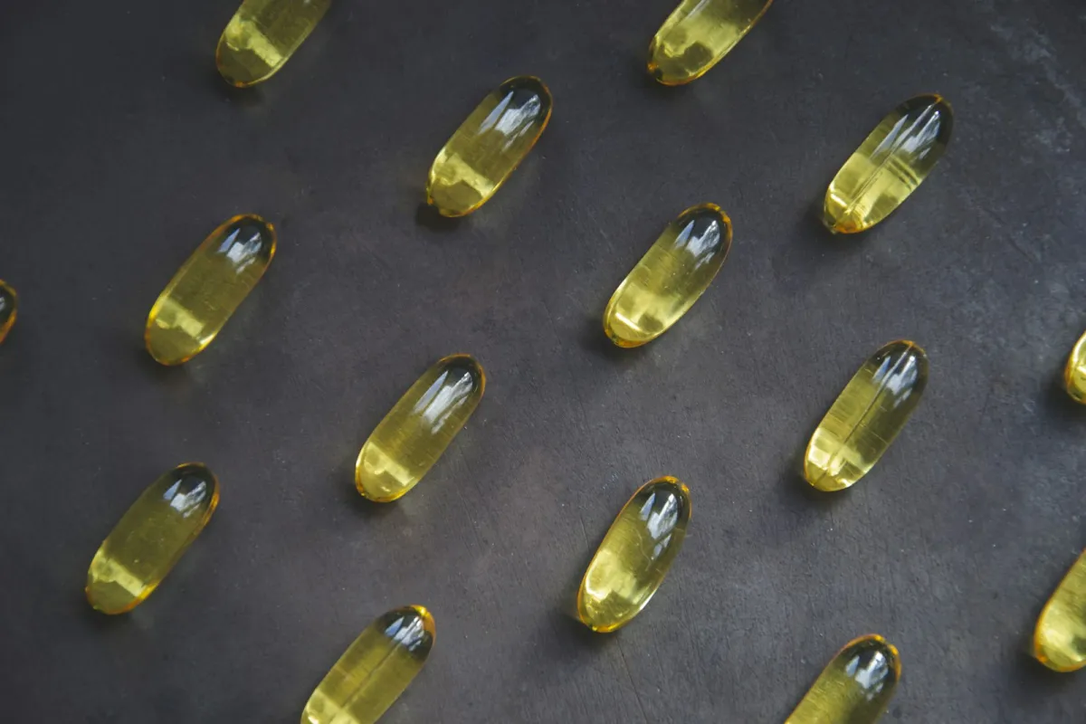 Rows of clear yellow softgel capsules on a dark slate surface