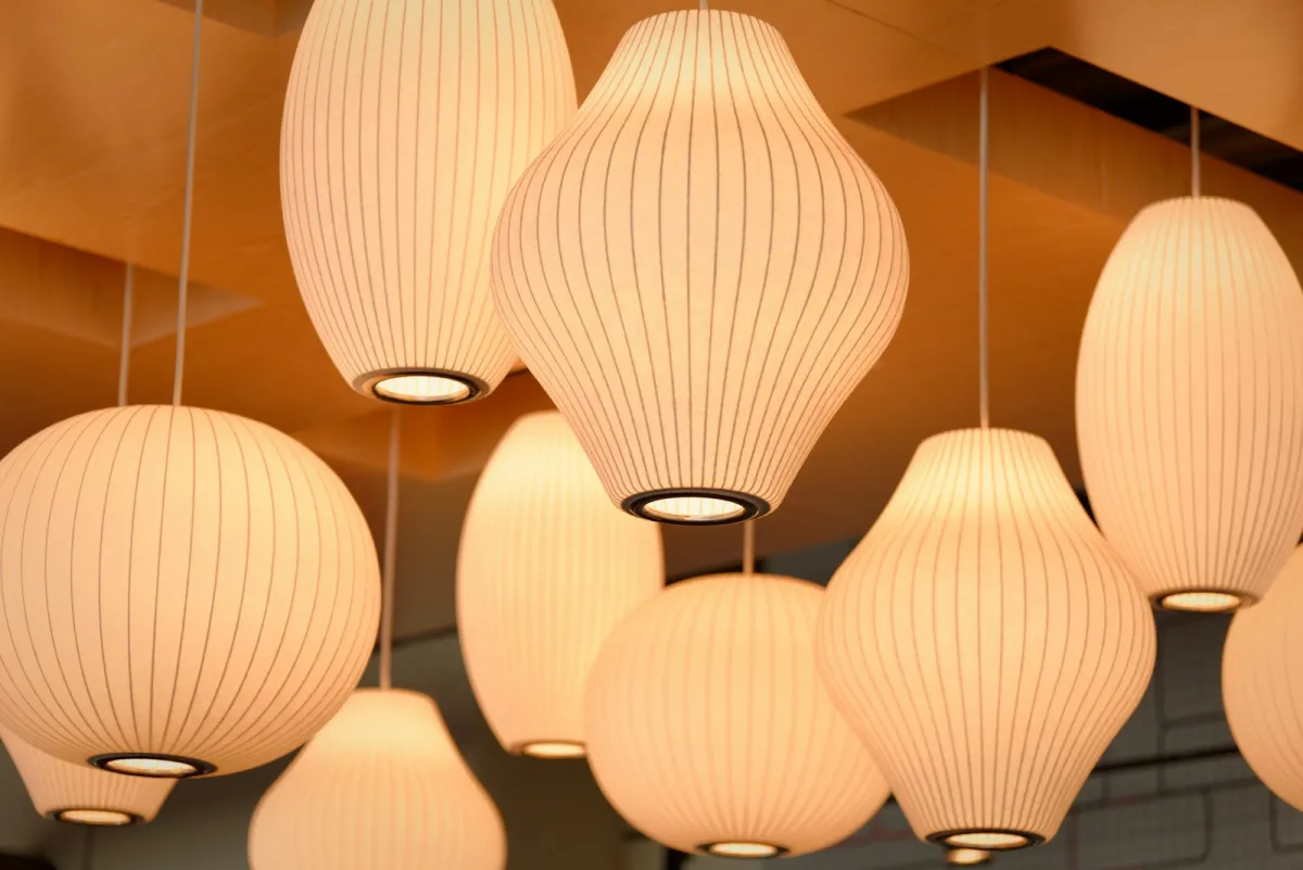 Cluster of white paper pendant lamps lit up beneath a wooden ceiling