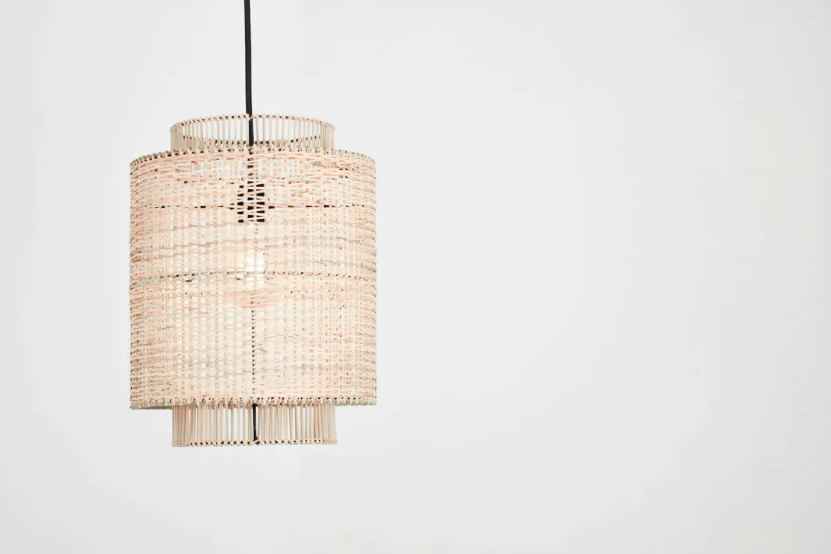 A woven rattan pendant lampshade hanging against a plain white wall A woven rattan pendant lampshade hanging against a plain white wall