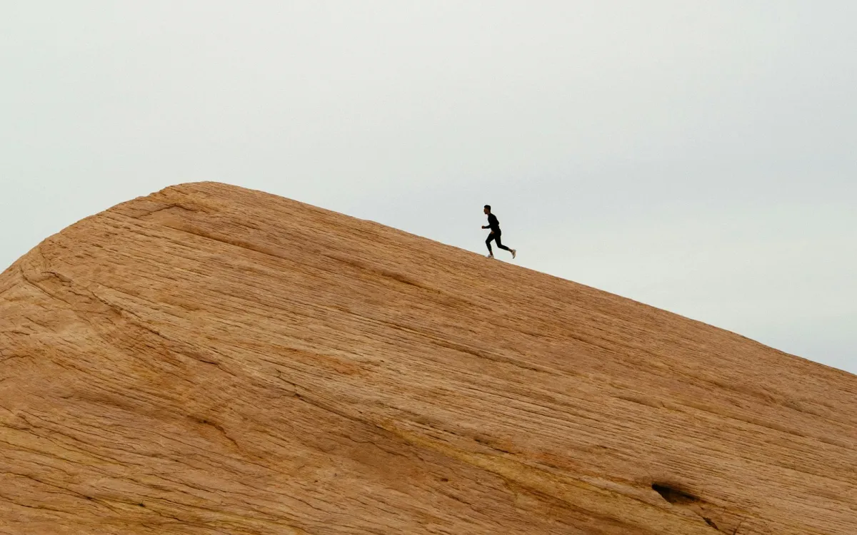 A lone runner silhouetted against a pale sky, running up a sweeping sandstone slope A lone runner silhouetted against a pale sky, running up a sweeping sandstone slope