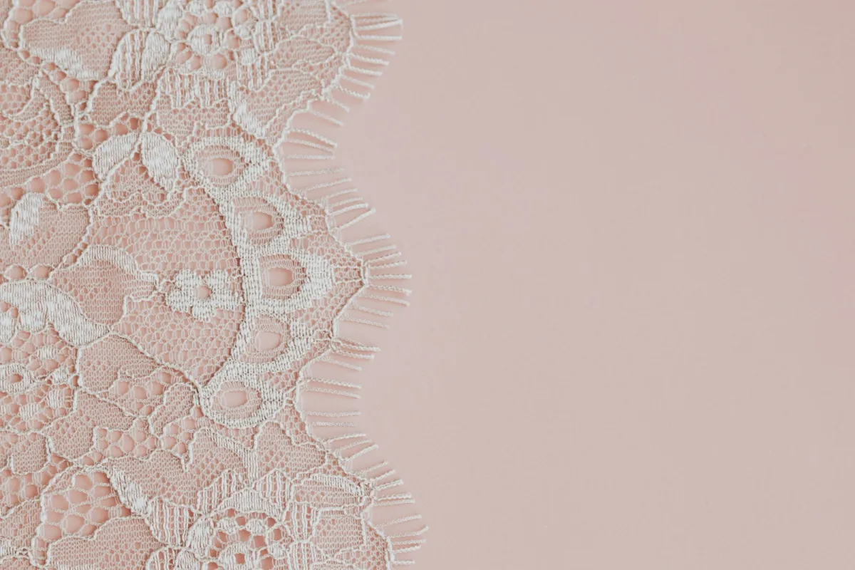 Delicate white lace fabric laid on a soft pink background